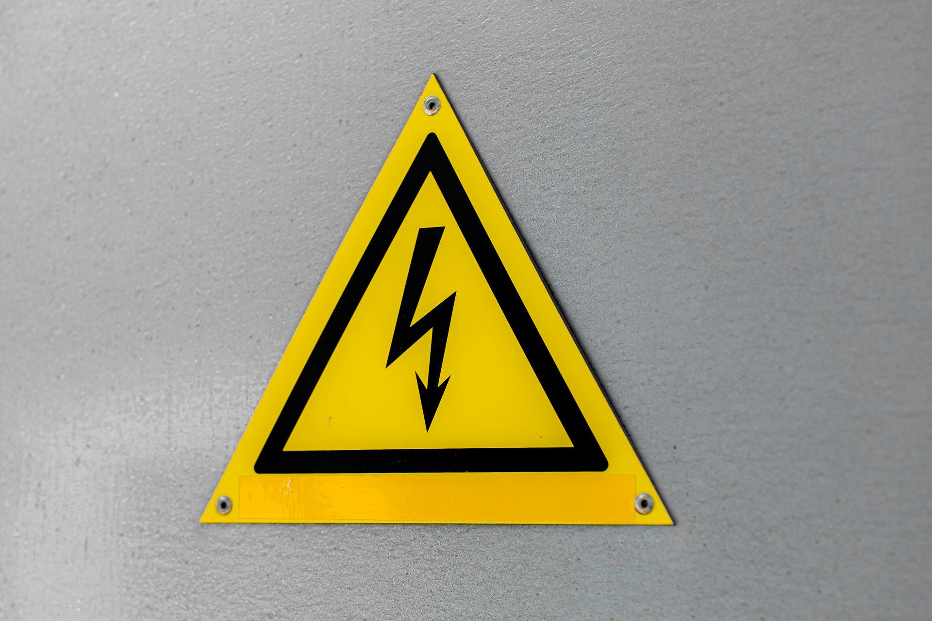 Close-up of a yellow high voltage warning sign mounted on a wall.